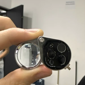 Lupa joyero plegable de metal con múltiples lentes y tornillos visibles, sostenida por mano.