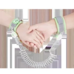 Manos de adulto y niño sujetas con arnés anti-pérdida verde con dinosaurio, cable en espiral blanco.