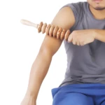 Hombre usa rodillo masajeador de madera en brazo para liberar tensión muscular.