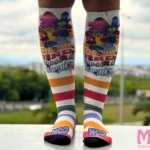 Medias de compresión tobillo-pantorrilla blancas con personajes animados, rayas de colores y logo "Mco Salud para tus Piernas".