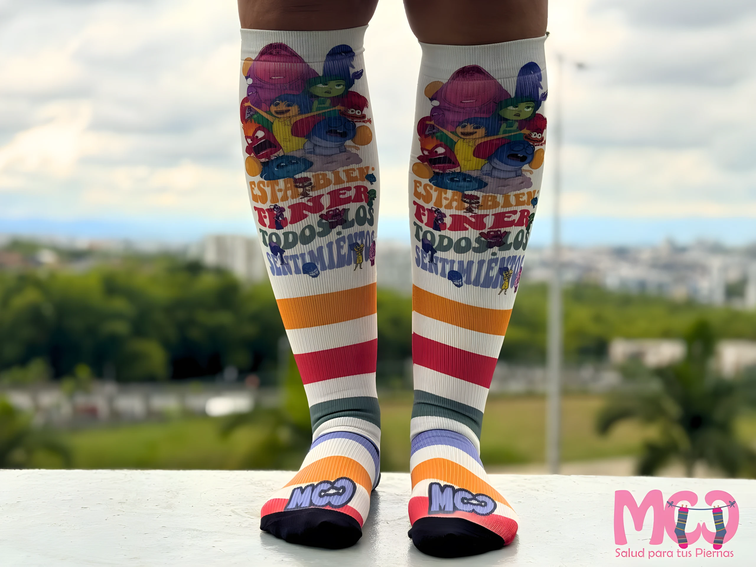 Medias de compresión tobillo-pantorrilla blancas con personajes animados, rayas de colores y logo "Mco Salud para tus Piernas".