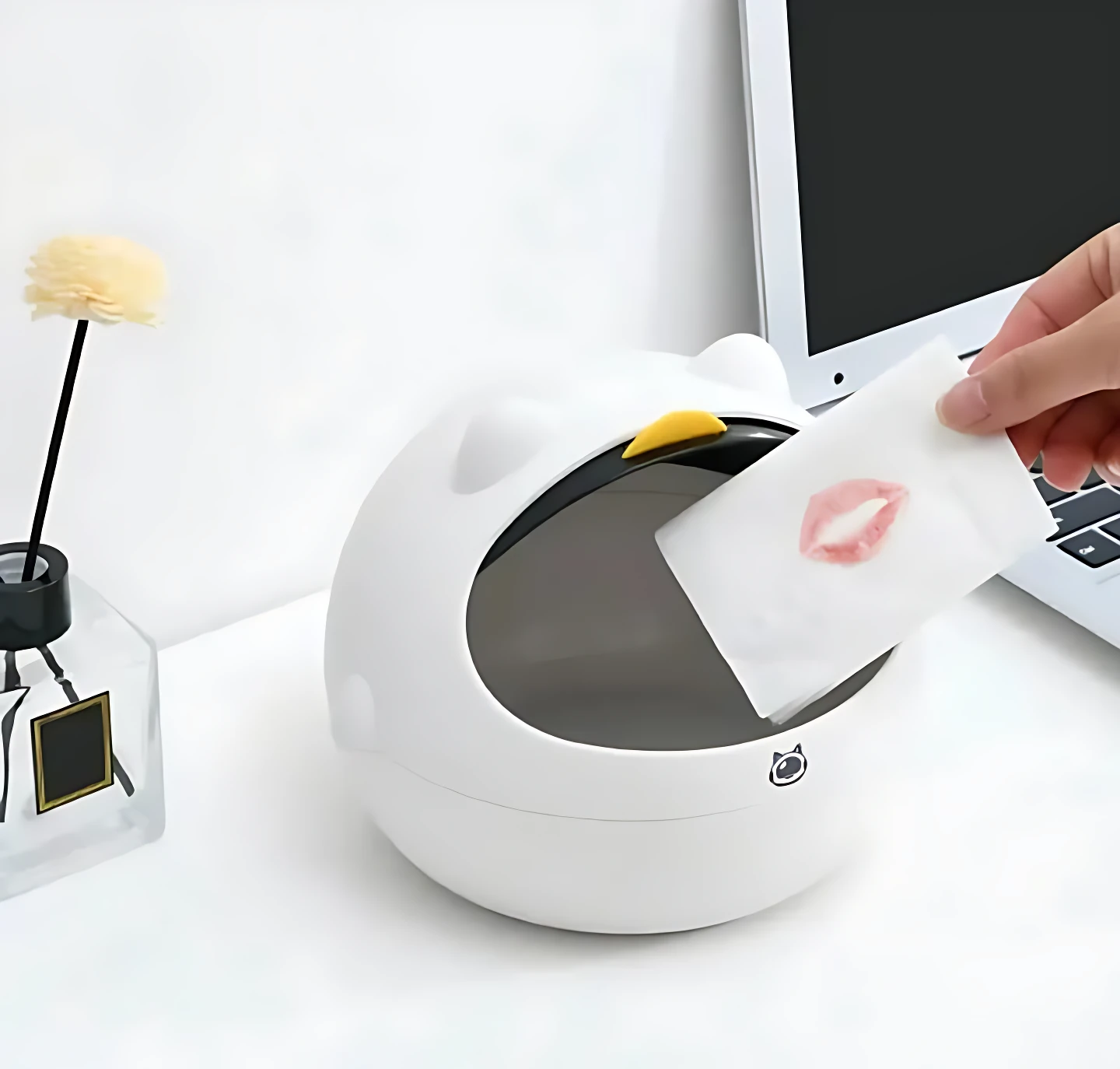 Mini basurero blanco con diseño de gato, tapa superior amarilla, para escritorio. Mano deposita pañuelo con labial.