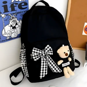 Mochila escolar negra con oso de peluche, lazo a cuadros y detalle de conejo en póster azul.