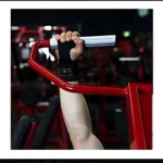 Muñequeras de gym negras, detalle logo blanco, mano sujetando barra de pesas, equipo rojo en fondo.