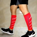 Pantorilleras de compresión running rojas con líneas blancas reflectantes, calzado deportivo negro.