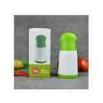 Picadora manual de hierbas verde y blanca, junto a su caja y verduras.