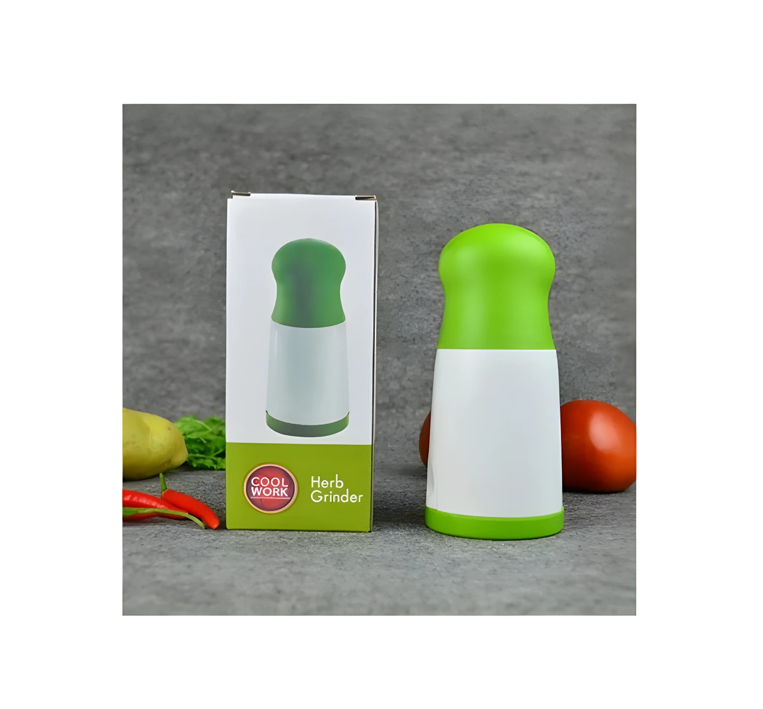 Picadora manual de hierbas verde y blanca, junto a su caja y verduras.