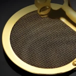 Pinzas de cocina doradas en primer plano con escurridor de malla fina, detalle de diseño.