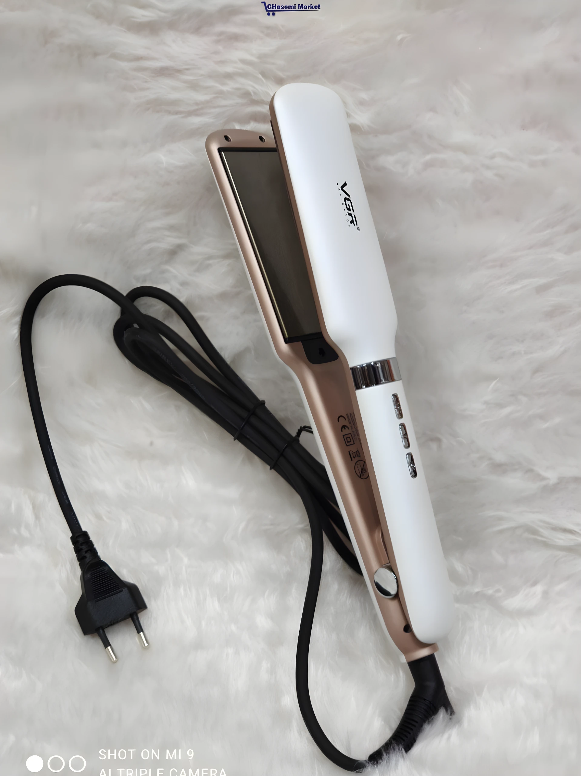 Plancha alisadora VGR blanca con bordes dorados y cable negro, apoyada sobre una superficie de peluche blanca, mostrando placas lisas y control térmico.