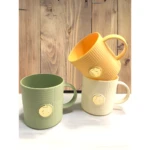 Set de 2 pocillos de cocina verdes y crema con relieve y sello dorado, ideales para café o té.