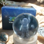 Esferas de cristal con astronautas 3D sobre bases de madera, junto a caja y cable blanco.