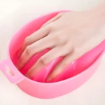 Recipiente rosado para manicure con diseño ergonómico y soporte interior para apoyar los dedos mientras se remojan las uñas en el tratamiento de belleza.