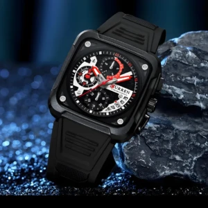 Reloj Curren cronógrafo negro, esfera con detalles rojos, correa de silicona, sobre rocas oscuras.
