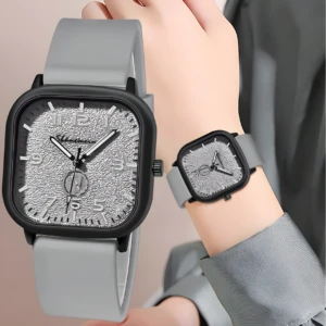 Reloj analógico unisex con caja cuadrada negra, dial gris texturizado y pulso de silicona gris, exhibido en primer plano y en una muñeca.