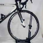 Bicicleta de ruta BH Carbono negra y blanca sobre soporte, enfocada en el frontal y rueda delantera.