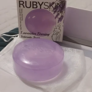 Jabón íntimo Rubyskin lavanda firmeza con niacinamida en empaque y suelto sobre malla.