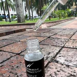 Serum aclarante Hobem Premium, gota de producto cayendo sobre frasco, en mesa de ladrillos.