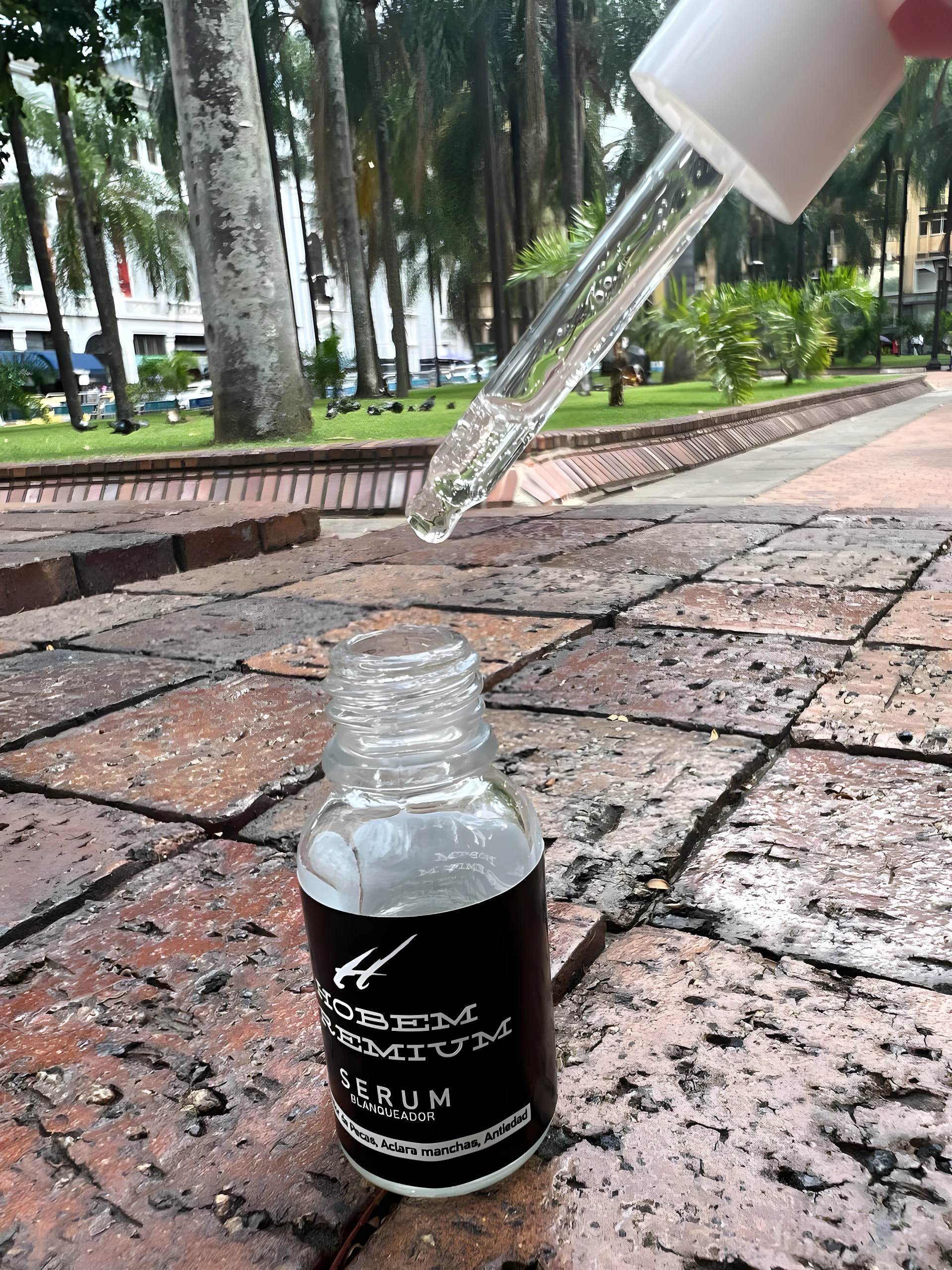 Serum aclarante Hobem Premium, gota de producto cayendo sobre frasco, en mesa de ladrillos.