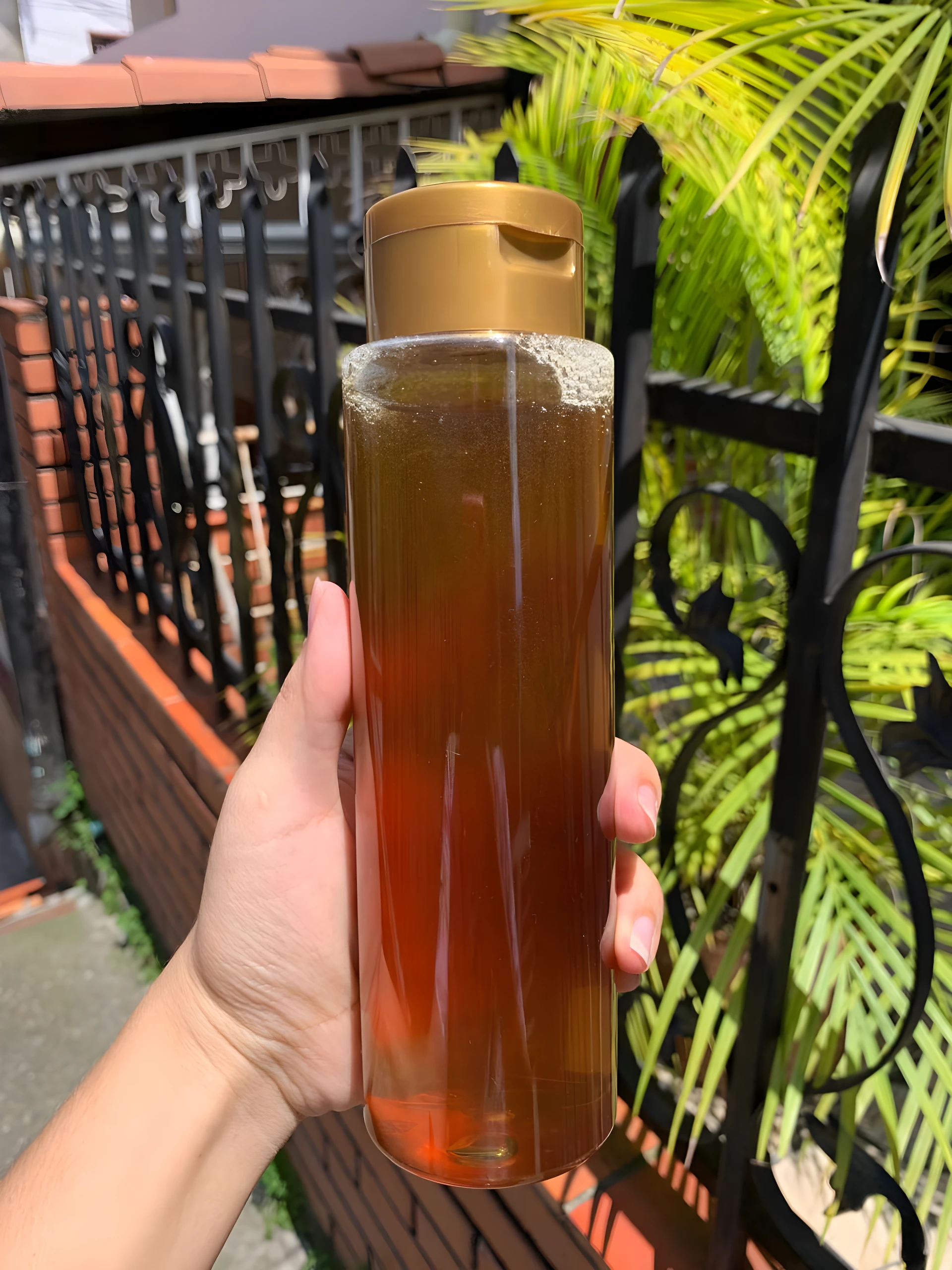 Botella con shampoo artesanal dorado, ideal para realzar reflejos en cabello claro, sostenida por mano con fondo exterior.