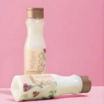 Dos botellas de shampoo Milagros de arroz con ácido hialurónico sobre fondo rosa, una de pie y otra acostada.