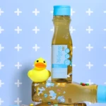 Shampoo Milagros Kids en botella con patito de hule amarillo y tres cápsulas verdes y rojas.