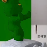 Soporte para celular verde con orejas doradas, sobre base gris texturizada de forma irregular, ideal para exhibir o sostener dispositivos.