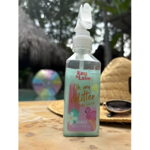 Splash corporal Key to Love 100ml con glitter, líquido azul claro en frasco rectangular con atomizador, frente a una piscina, sombrero y gafas de sol.