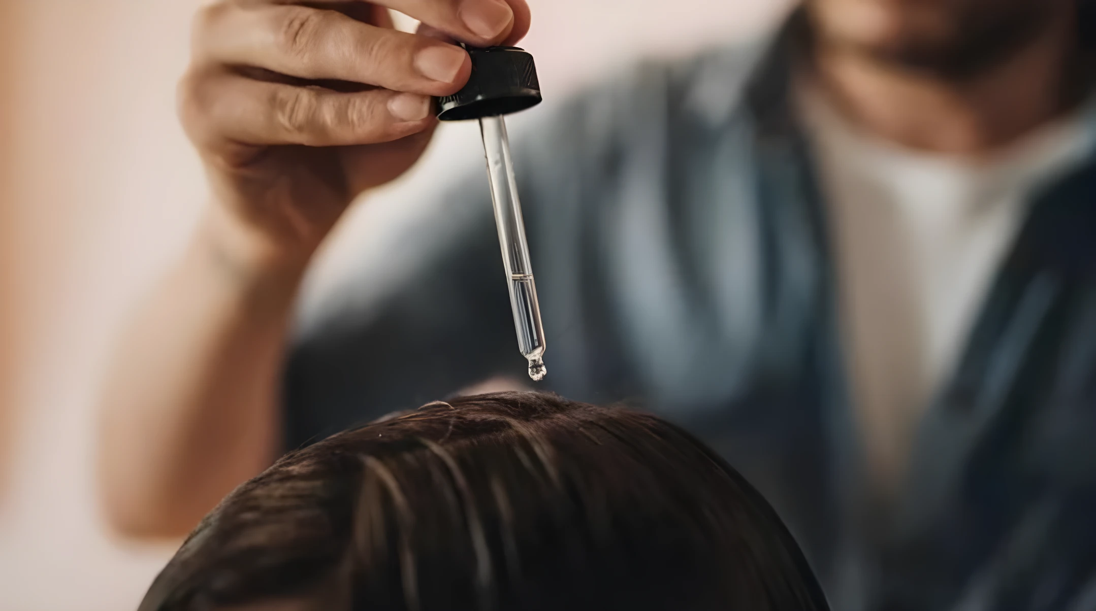 Mano aplicando suero capilar anti-piojos transparente directamente sobre el cuero cabelludo mediante un gotero de vidrio con tapa negra.
