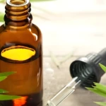 Frasco de vidrio ámbar con suero capilar y gotero separado sobre superficie de madera, rodeado de hojas verdes frescas para resaltar el origen natural.