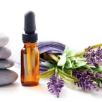 Frasco de vidrio ámbar con gotero junto a piedras zen apiladas y flores de lavanda, ideal para exhibir set de suero capilar anti-piojos.