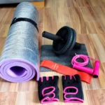 Kit de entrenamiento: tapete morado, rueda abdominal, guantes negros/rosados, banda roja y cuerda de saltar rosa.