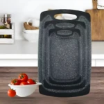 Tabla picadora gris con puntos blancos, encimera de cocina con tomates en cuenco blanco.