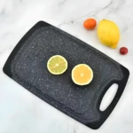 Tabla picadora negra granulada antideslizante con limón verde, amarillo y frutas rojas sobre fondo blanco.