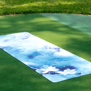 Tapete de yoga profesional azul con diseño de flores de loto, extendido sobre césped artificial.