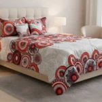 Tendido abullonado cama doble 1.40 con diseño circular rojo y gris, sobre cama de madera, junto a mesa de noche y lámpara.