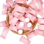 Toallas faciales compactas en empaque rosa individual, varias en cuenco de madera y sueltas.