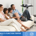 Familia disfrutando un proyector sobre un trípode ajustable con bandeja, un sofá blanco y una mesa de centro.