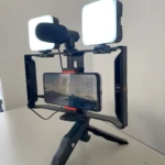 Trípode portátil negro con celular, micrófono y dos luces LED cuadradas para grabación.
