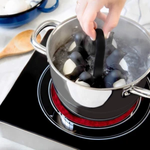 Organizador de huevos pingüino en olla hirviendo, ideal para cocinar huevos de forma segura y divertida.
