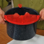 Colador Better Strainer rojo con diseño acanalado para ollas negras, sosteniéndolo con ambas manos.