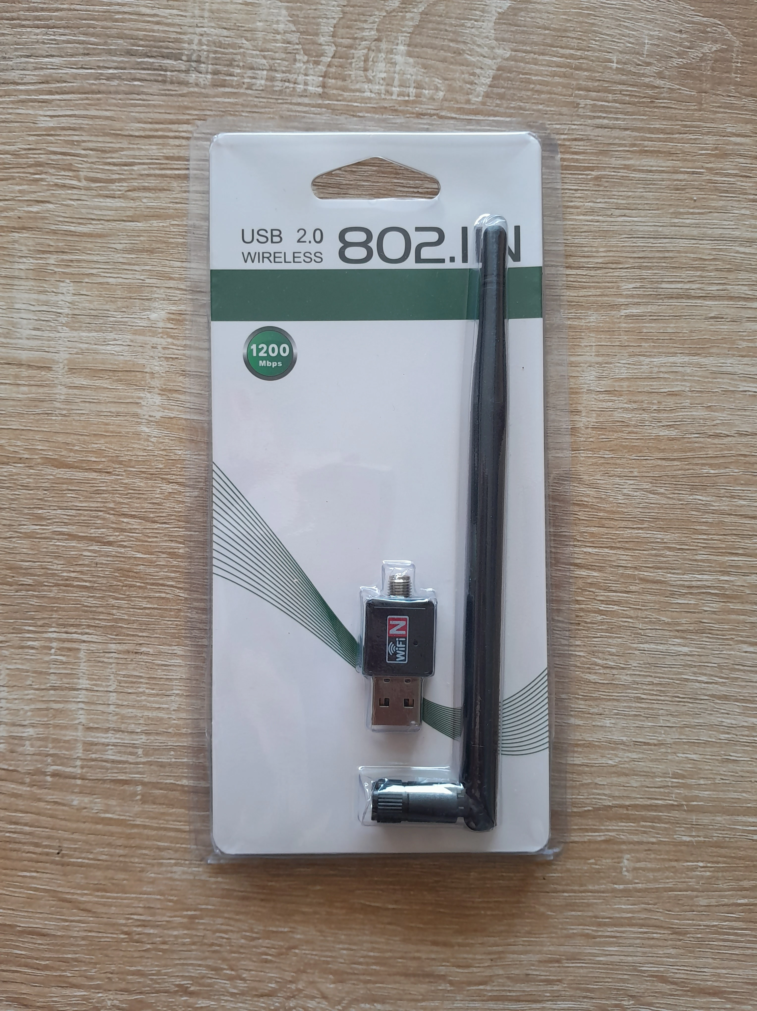 Antena WiFi USB 802.11n 1200 Mbps, conector giratorio y antena externa, en empaque de cartón y plástico.