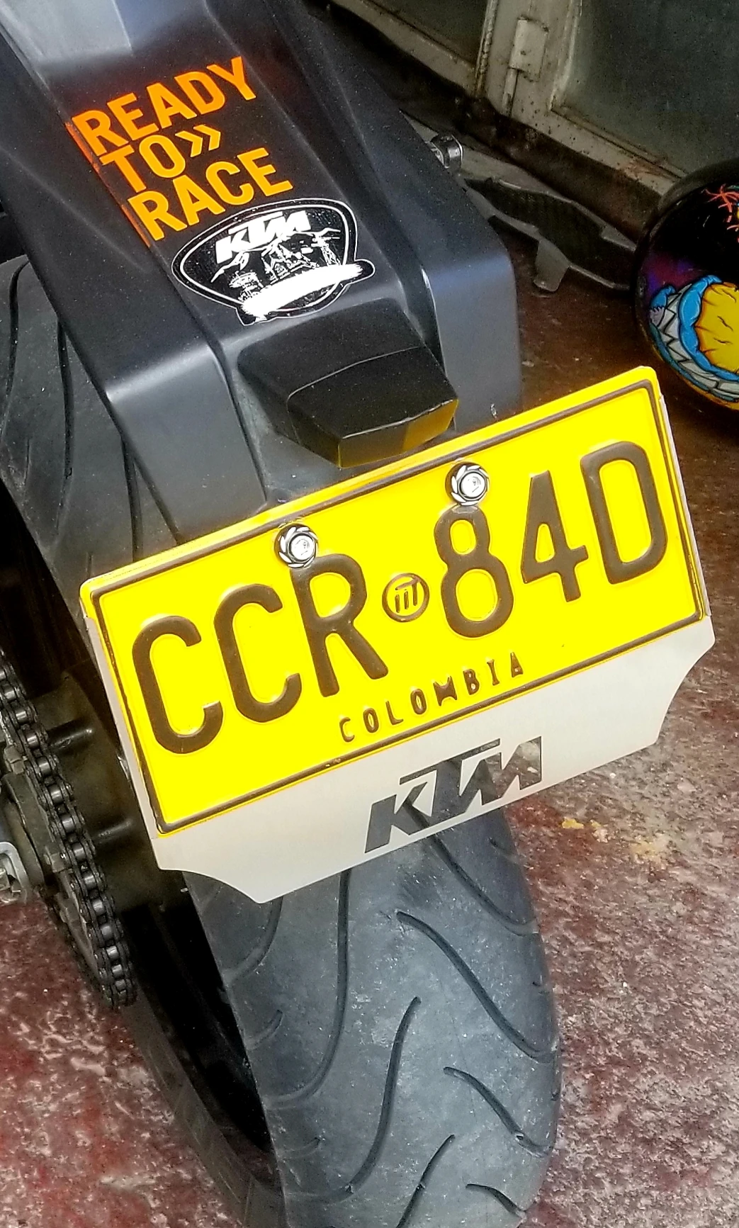 Porta placas de acero inoxidable para moto, color blanco con logo KTM visible en la parte trasera, instalado en la sección de la cola de una motocicleta negra.