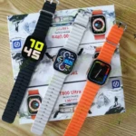 Smartwatch T800 Ultra negro, blanco y naranja con dos correas, sobre cajas de producto.