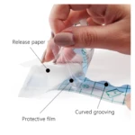 Mano separando la película protectora de un parche cicatrizante transparente con rejilla azul y canalado curvo para tatuajes.