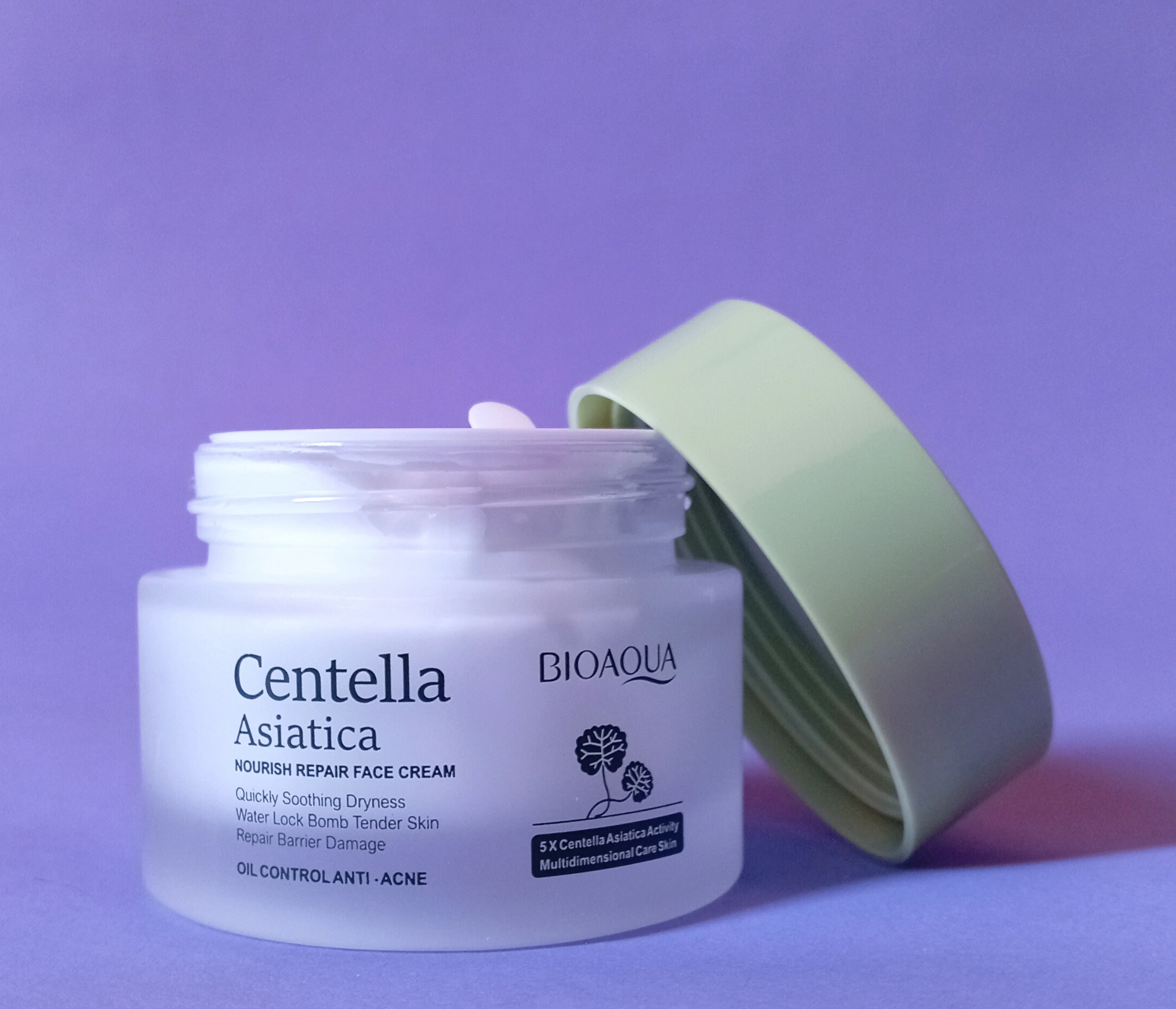 Crema facial Centella Asiática BIOAQUA en envase blanco translúcido con tapa verde claro abierta, fondo morado.