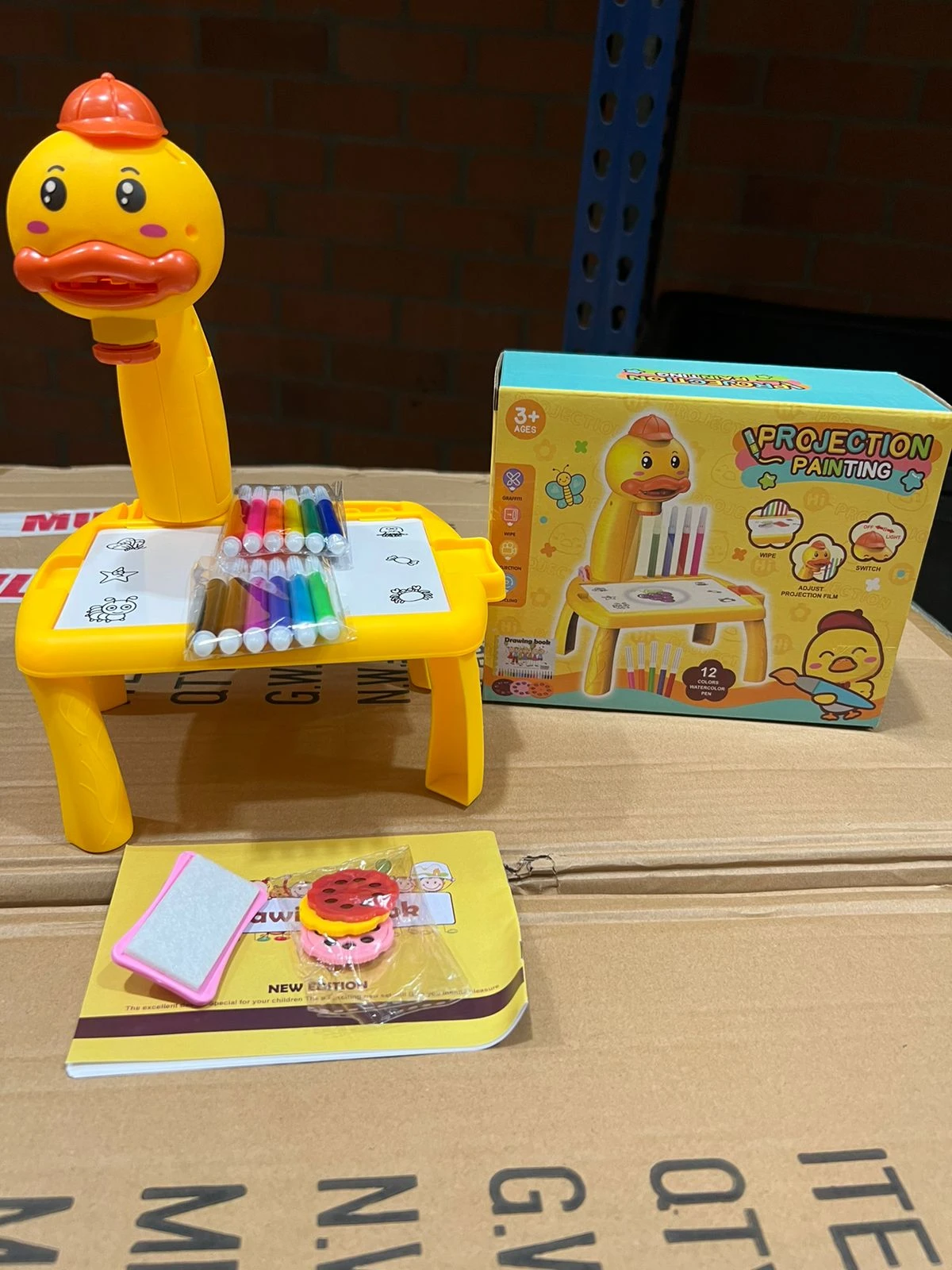 Escritorio amarillo con patas de goma, base rectangular y soporte para plumones. Incluye proyector de dibujos animados, caja original y accesorios en bolsa.