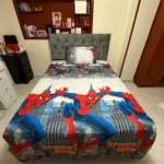 Sábana infantil Spiderman con estampado de superhéroe sobre fondo urbano, colocada en cama con cabecero gris y almohada blanca.