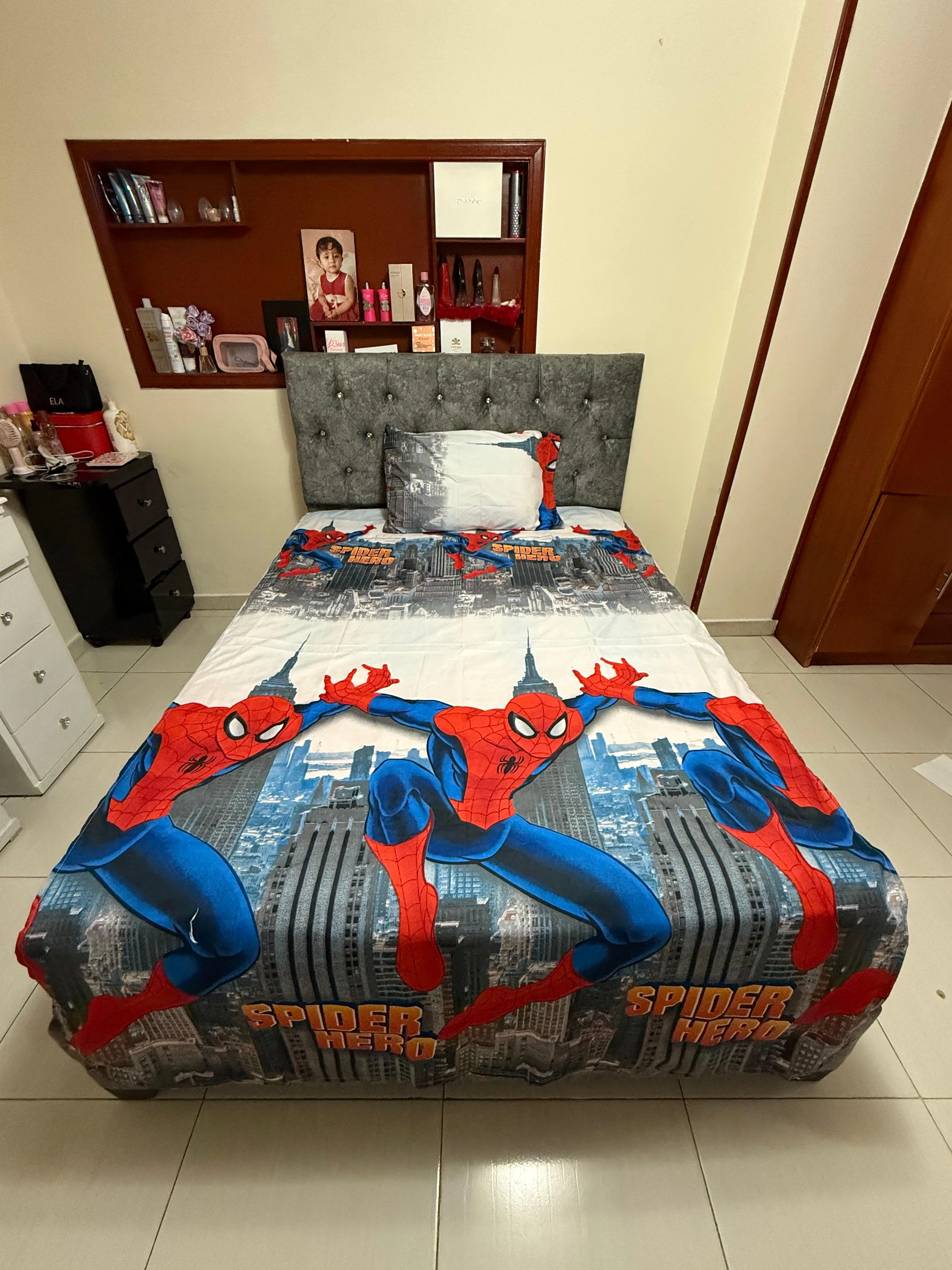 Sábana infantil Spiderman con estampado de superhéroe sobre fondo urbano, colocada en cama con cabecero gris y almohada blanca.