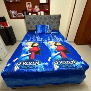 Sábana infantil Frozen de algodón suave, con estampado de Elsa y Anna en azul vibrante, sobre cama con cabecero tapizado gris.