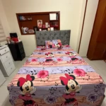 Sábana infantil piel de durazno con estampado de Minnie Mouse, colocada sobre cama con cabecero tapizado gris.